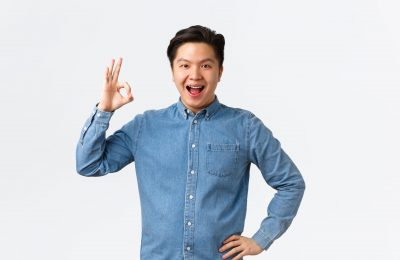 Satisfied confident smiling asian guy with braces, showing okay gesture, recommend perfect doctor clinic, great stomatology, being pleased with results, standing white background amazed.